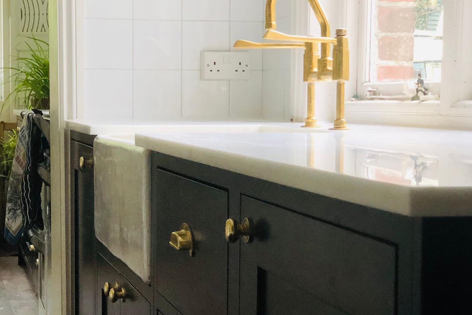 dark blue shaker style kitchen with traditional brass tap and white HiMacs worktop