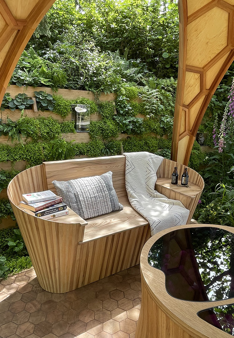 Chelsea flower show chanterelle mushroom bench with cushion, books and foliage behind