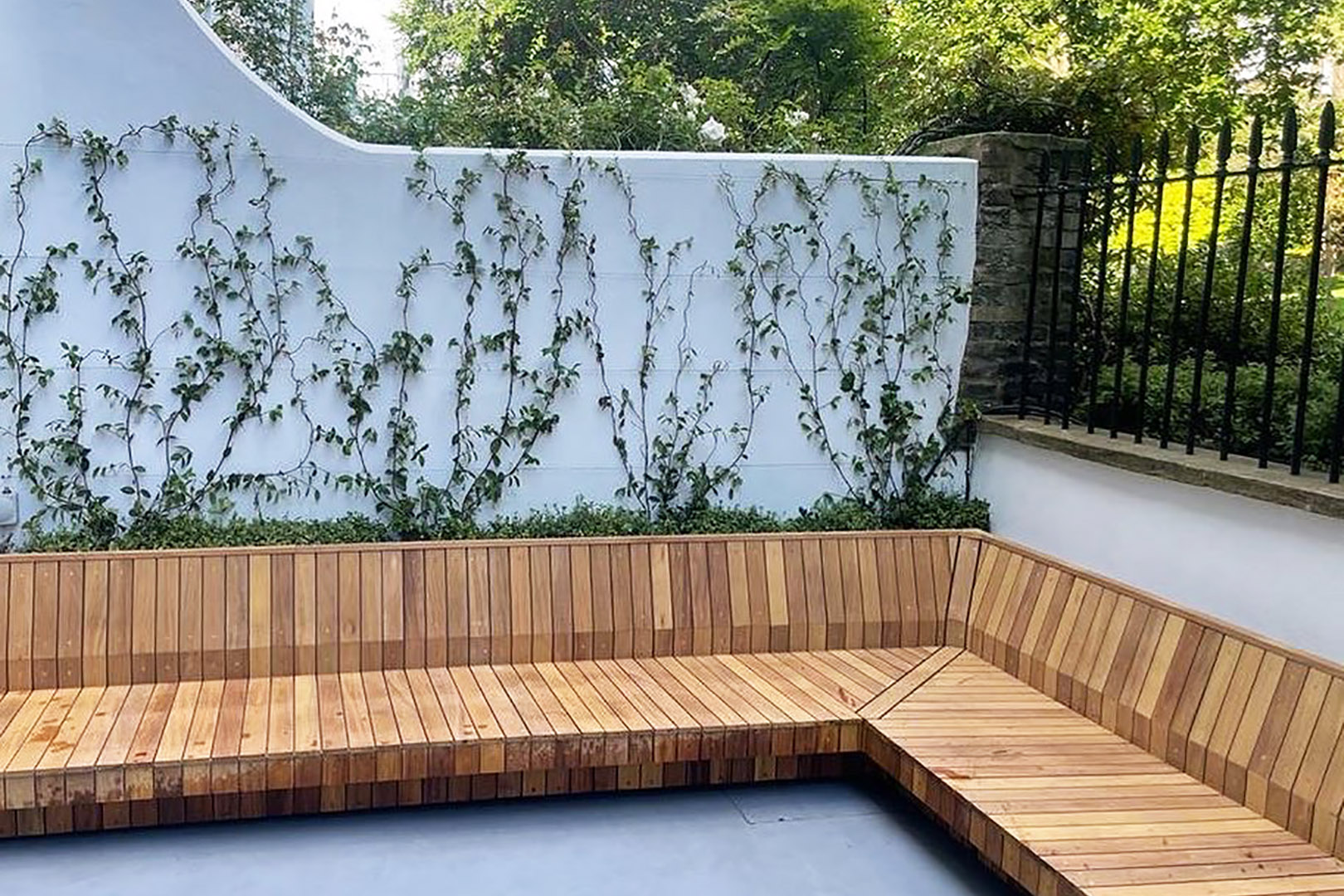 huge Iroko garden seat in a paved outdoor area with foliage growing up a white wall