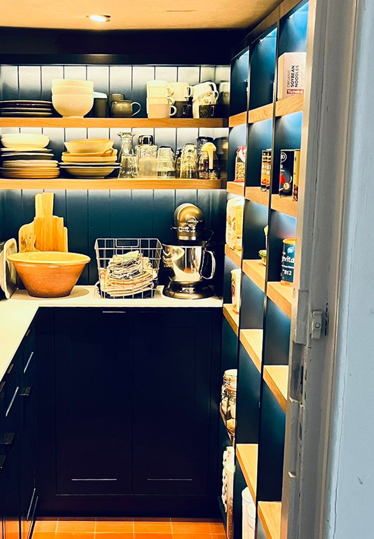 internal view of a dark blue kitchen pantry with white tops and oak shelves