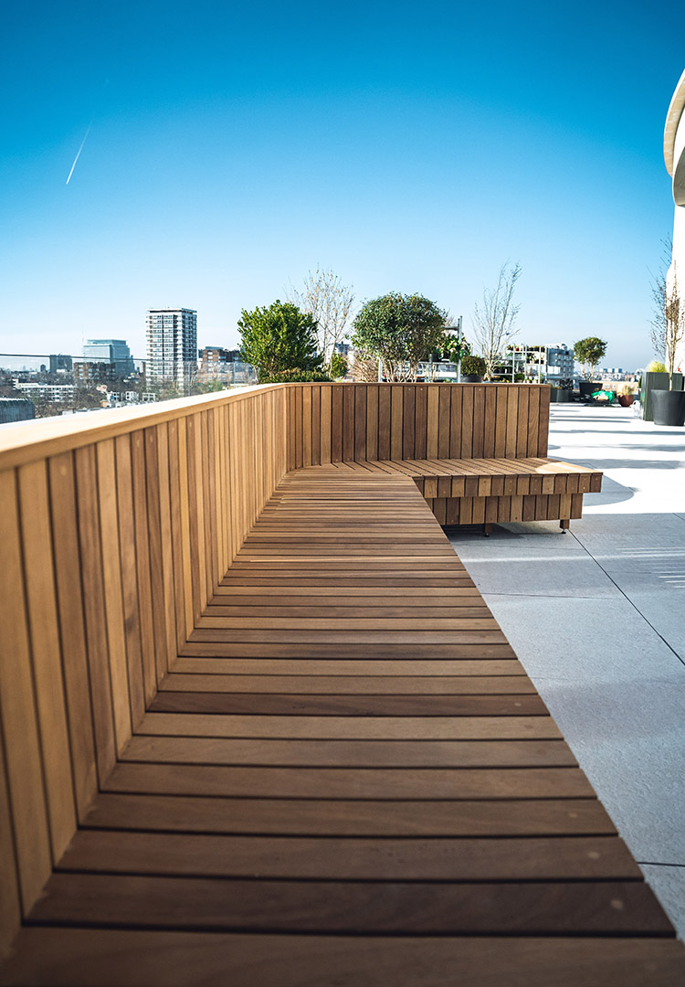 Side view of luxury outdoor furniture, Iroko slatted bench with a blue London skyline