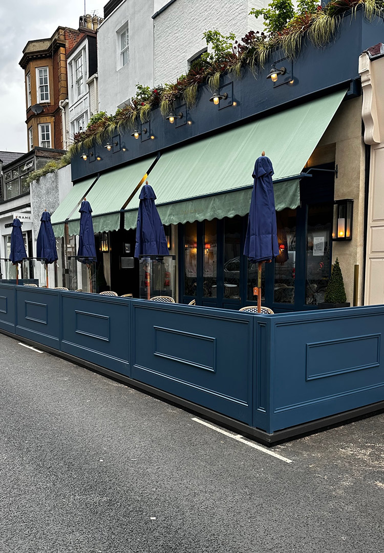 Full side view of the outdoor seating area of Daphne's Restaurant in Kensington, including partitions and parasols